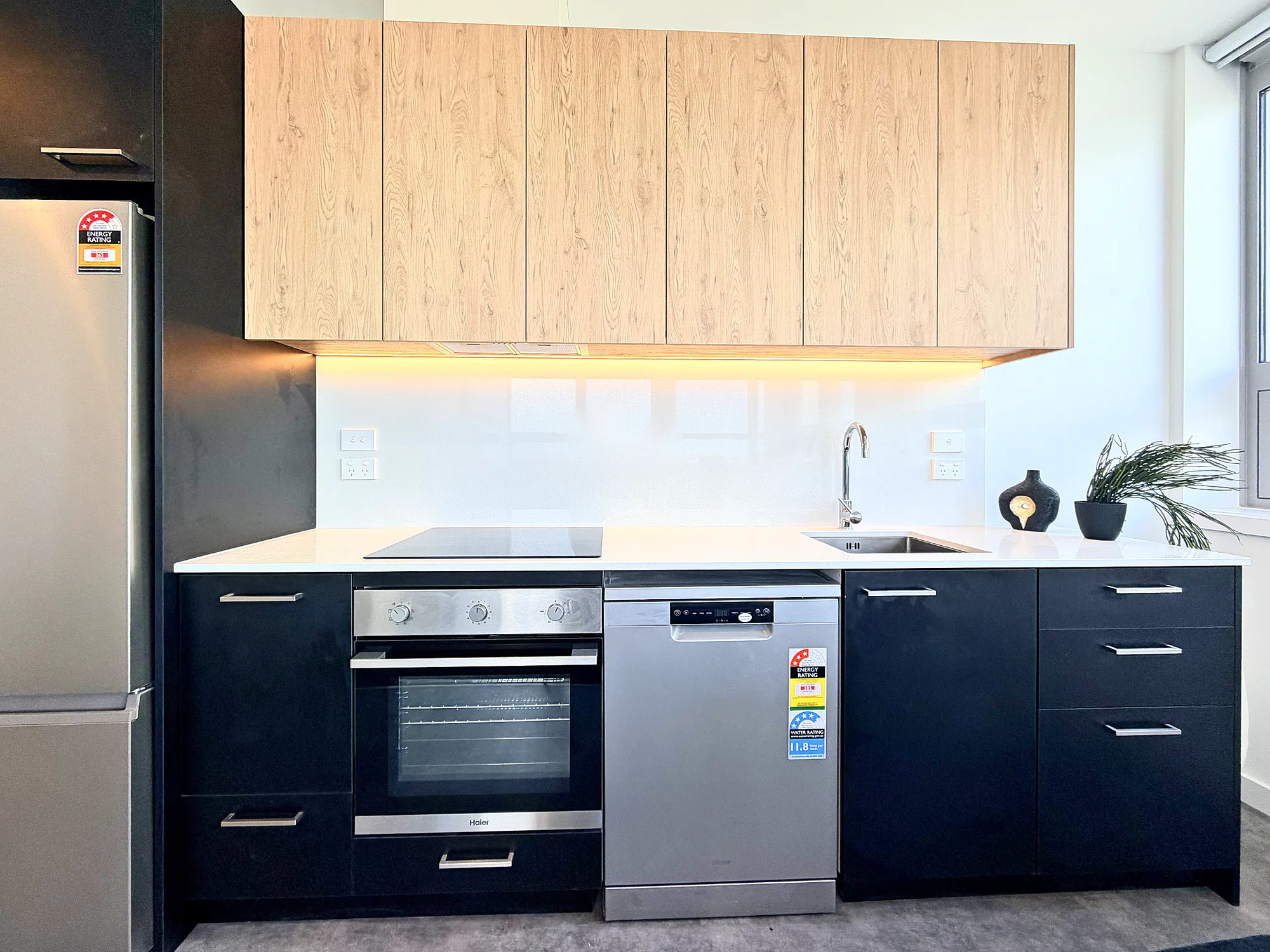 Kitchen with timber upper cabinets, dark joinery, oven and dishwasher in a two bedroom corner display home at Avalon Apartments, Lower Hutt