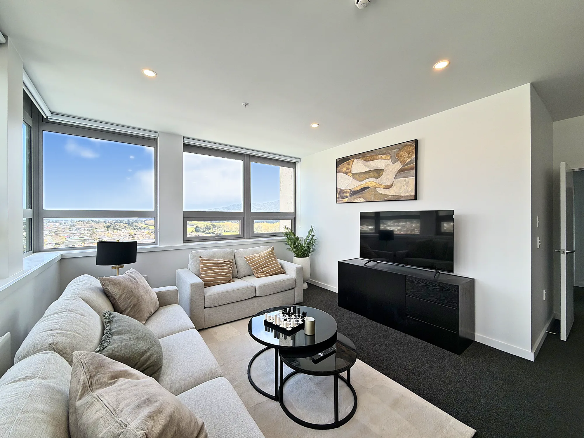 Living room with sofas, television and wide windows in a two bedroom corner display home at Avalon Apartments, Lower Hutt